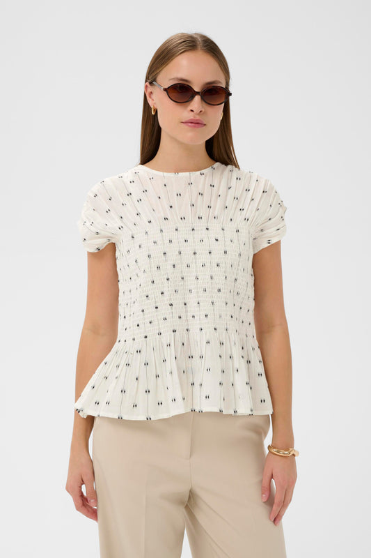 Woman wearing the Soaked in Luxury Amelie white blouse with black dots and ruffled details.