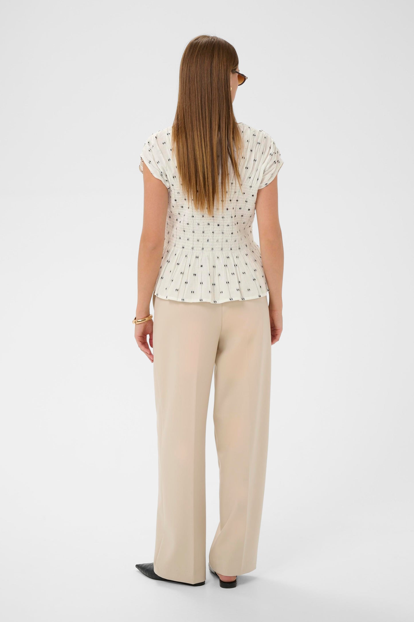 Woman wearing the Soaked in Luxury Amelie white blouse with black dots and ruffled details.
