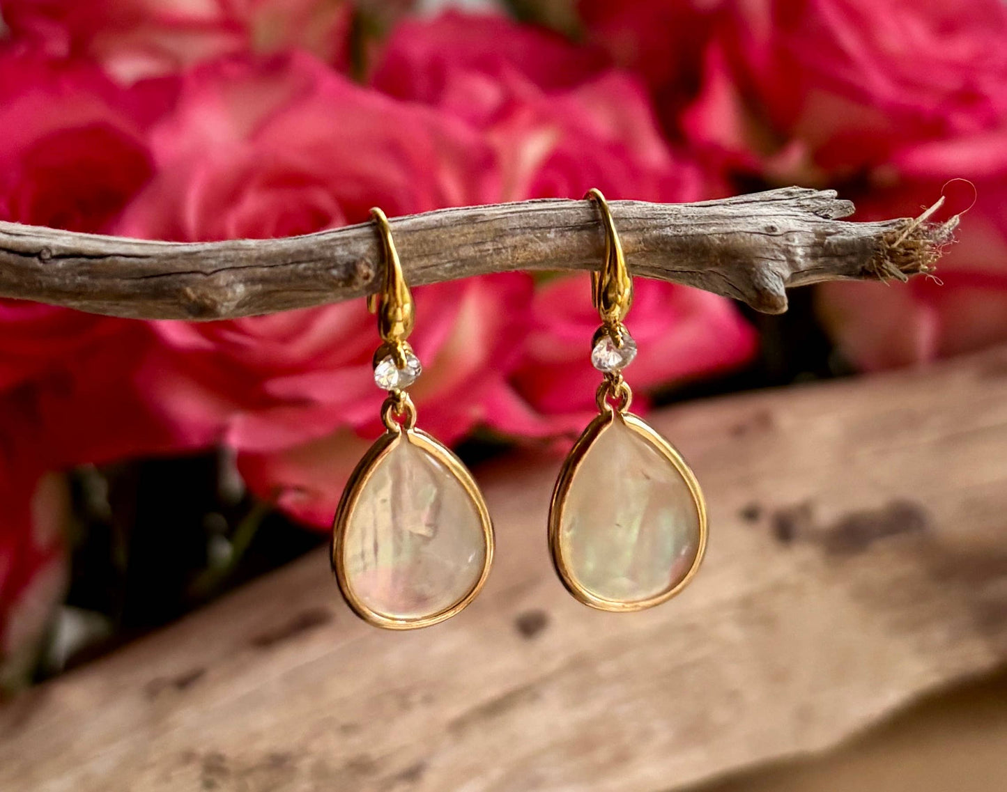 Gold teardrop earrings with mother of pearl on a branch with pink flowers in the background