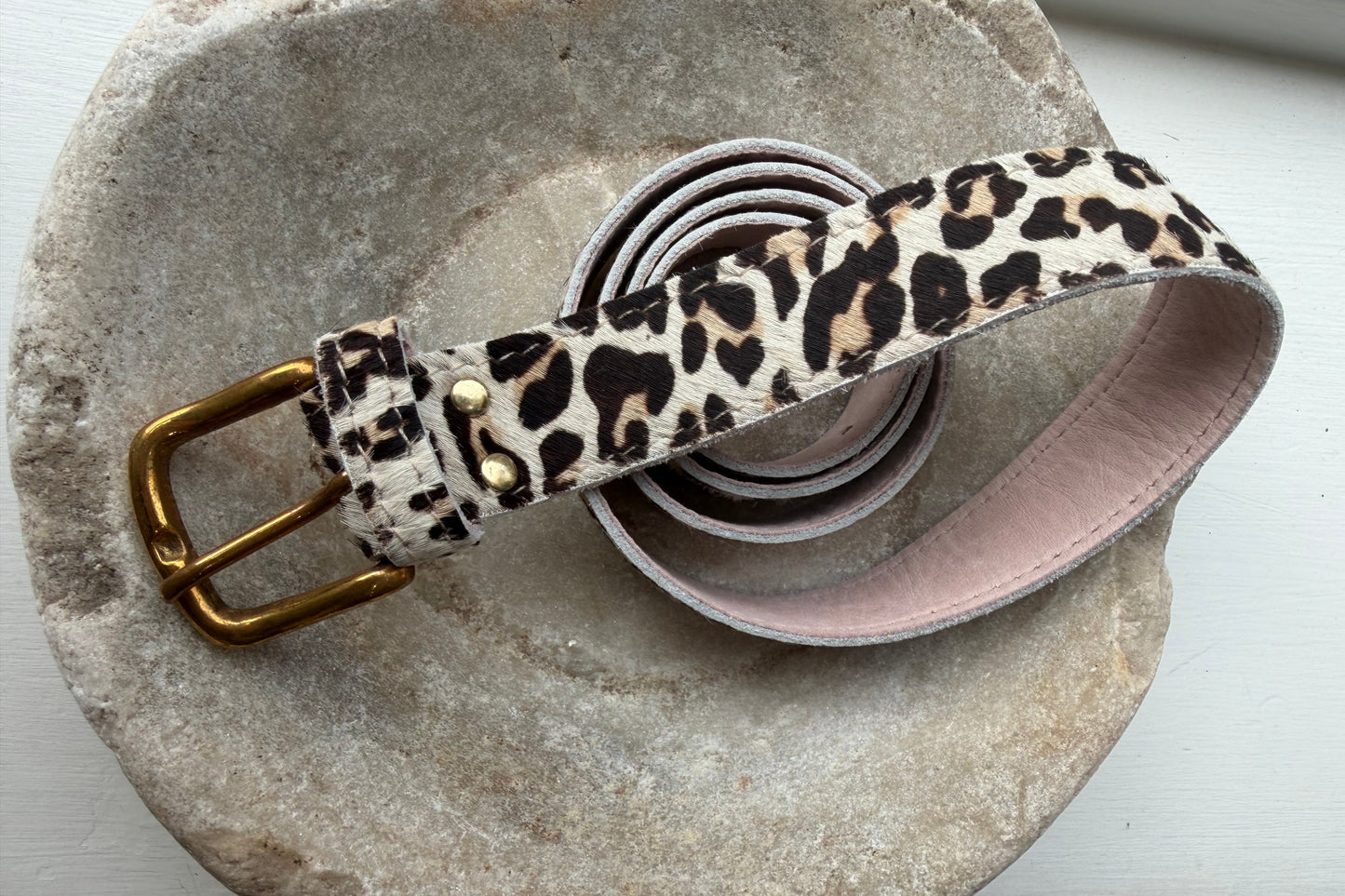 Leopard print belt with a gold buckle on a stone surface