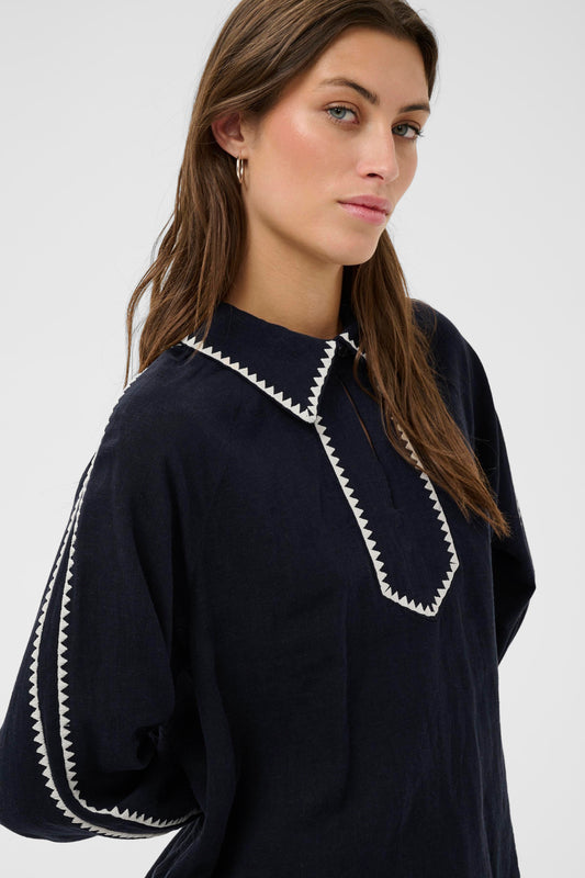 Woman wearing the part two Aimy Linen blend navy blouse with white trim and white pants on a white background
