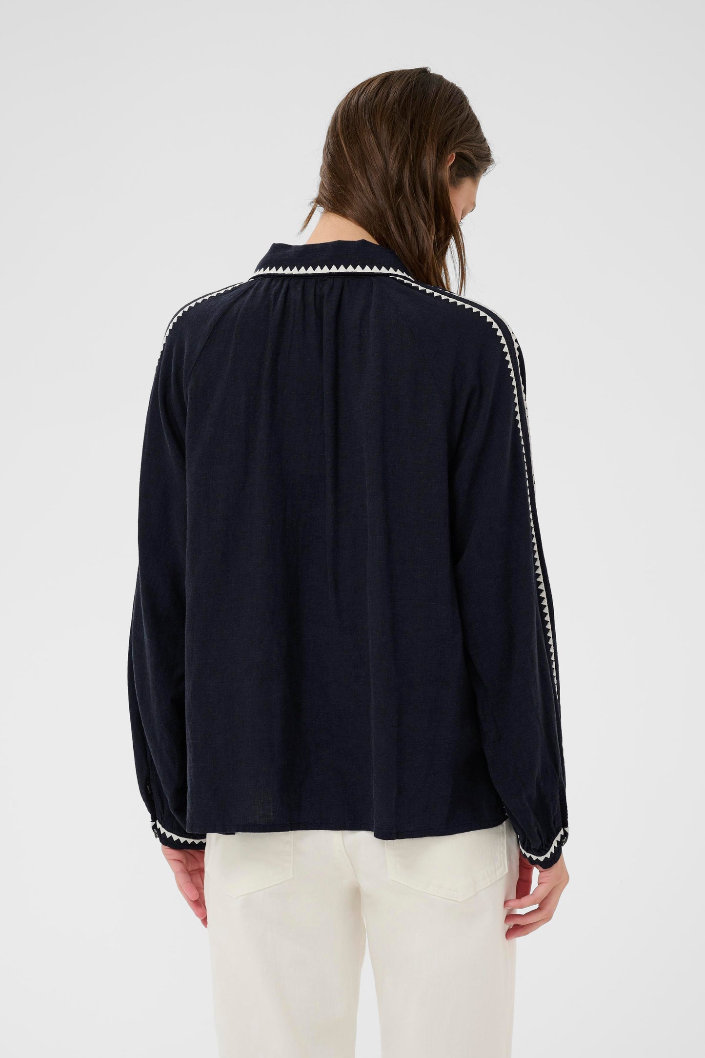 Woman wearing the part two Aimy Linen blend navy blouse with white trim and white pants on a white background