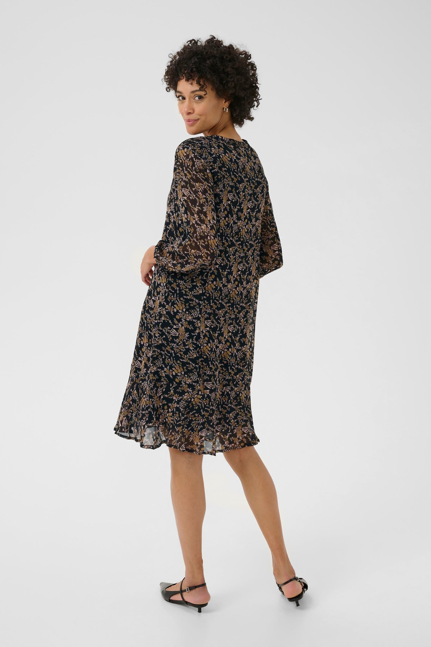 Woman wearing a floral dress on a white background. View is taken from behind