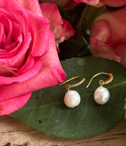 Gold earrings with white pearls on a green leaf next to pink roses