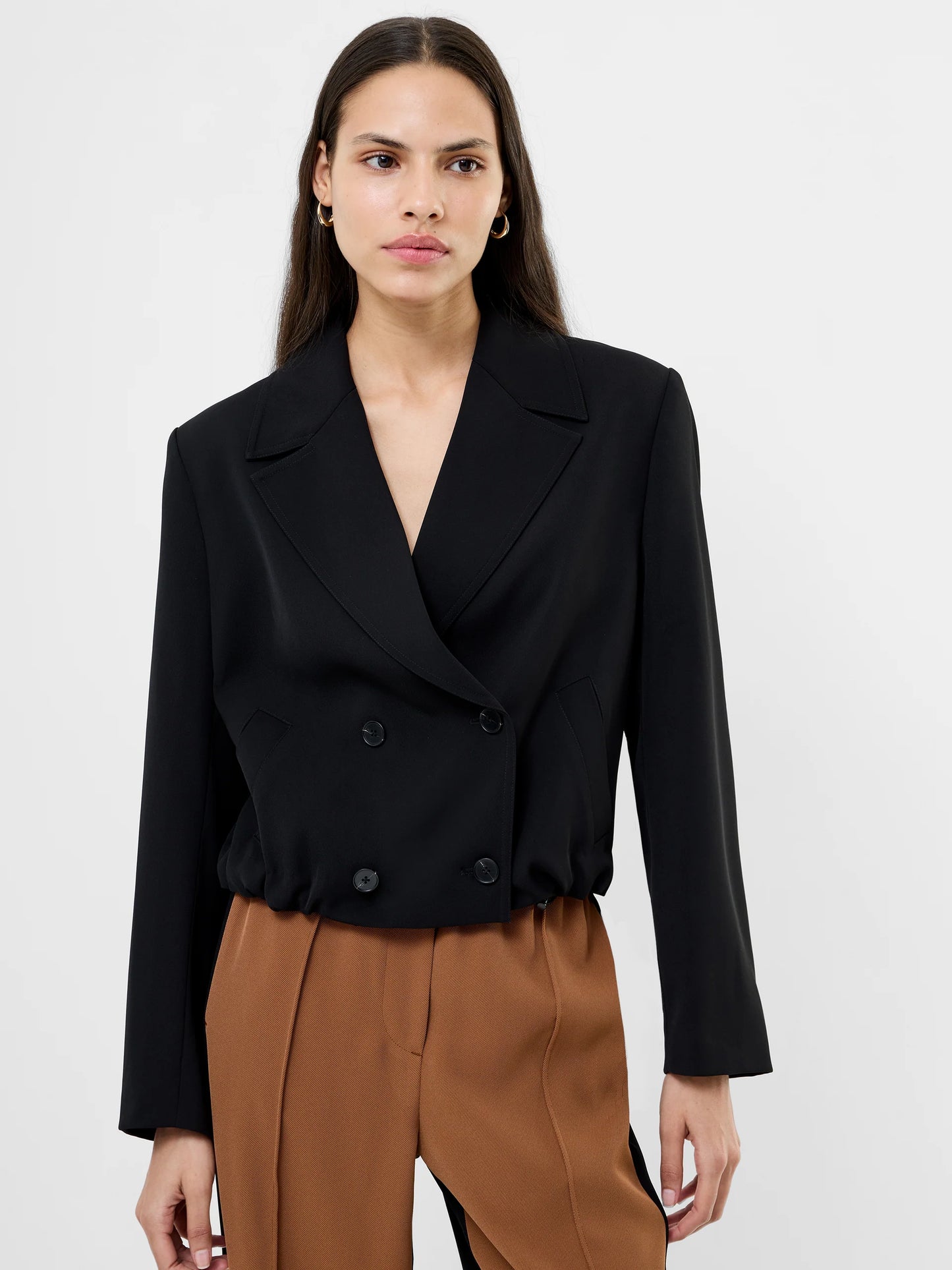 Women wearing a black cropped suit jacket with collar, 4 double breasted buttons and ruched bottom to jacket.