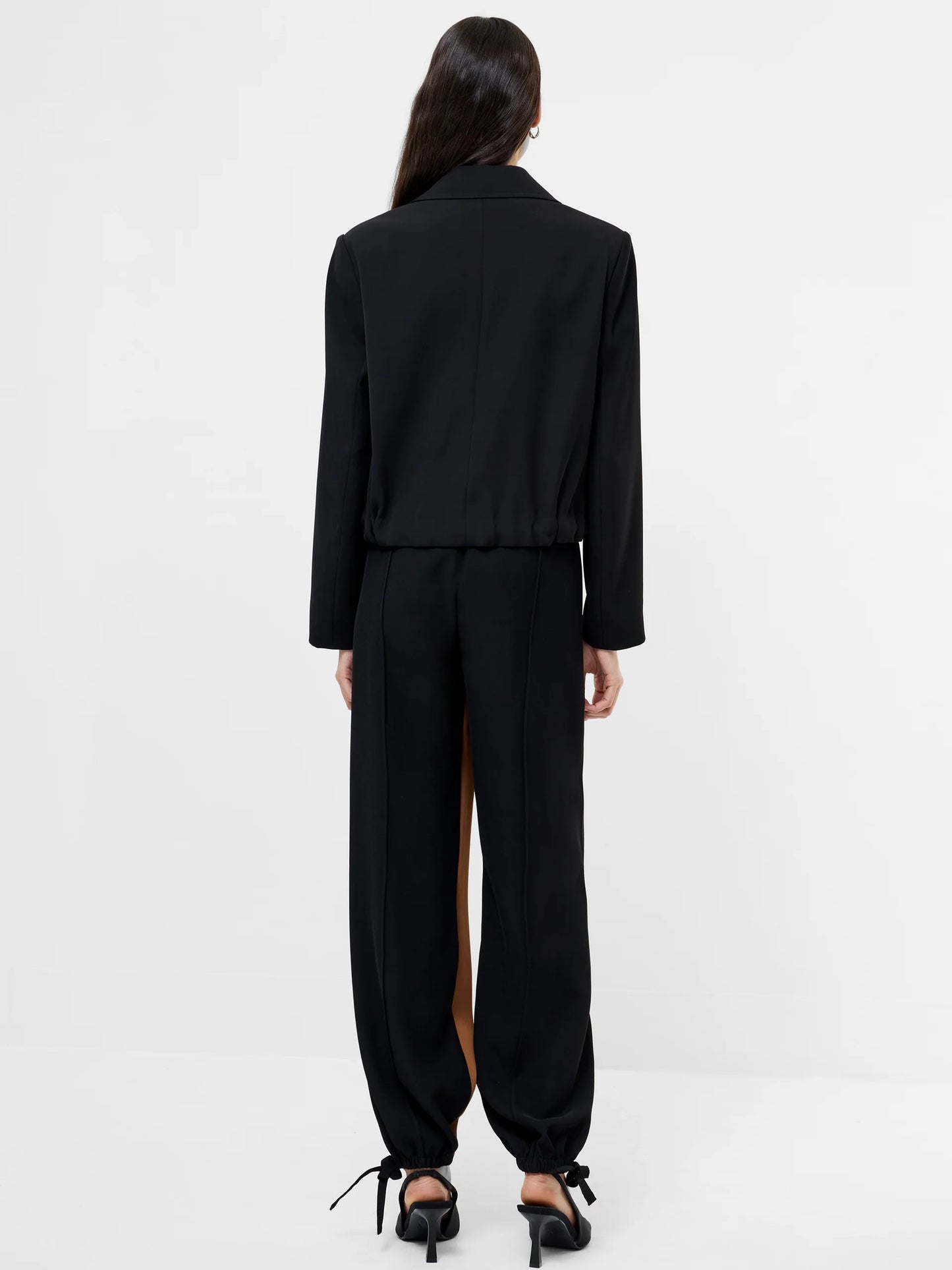 Women wearing a black cropped suit jacket with collar, 4 double breasted buttons and ruched bottom to jacket. Back View