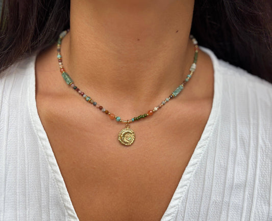 Necklace with colorful beads and a gold pendant worn by a person in a white top.