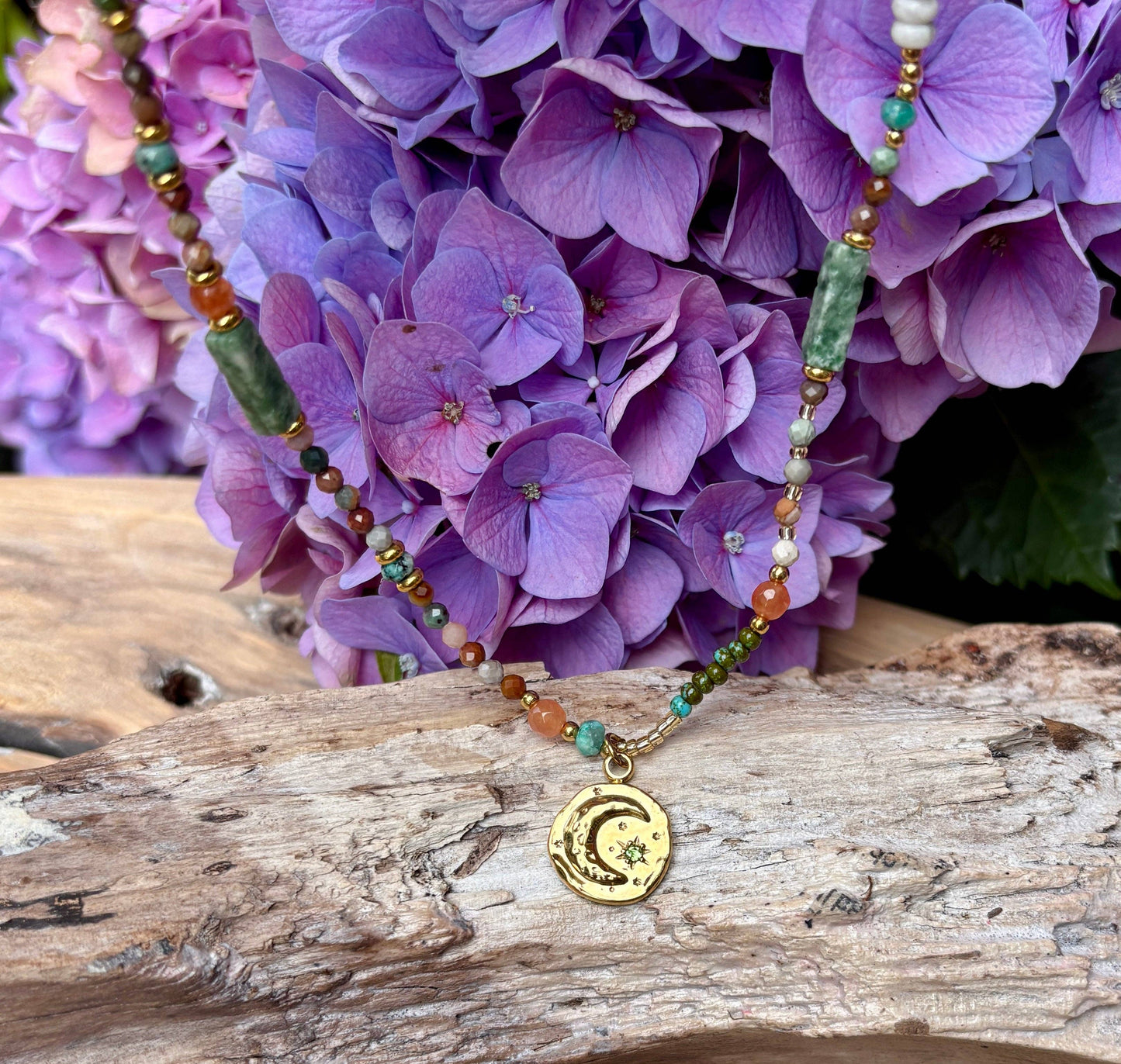 Necklace with a moon and star pendant on a wooden surface with purple flowers in the background