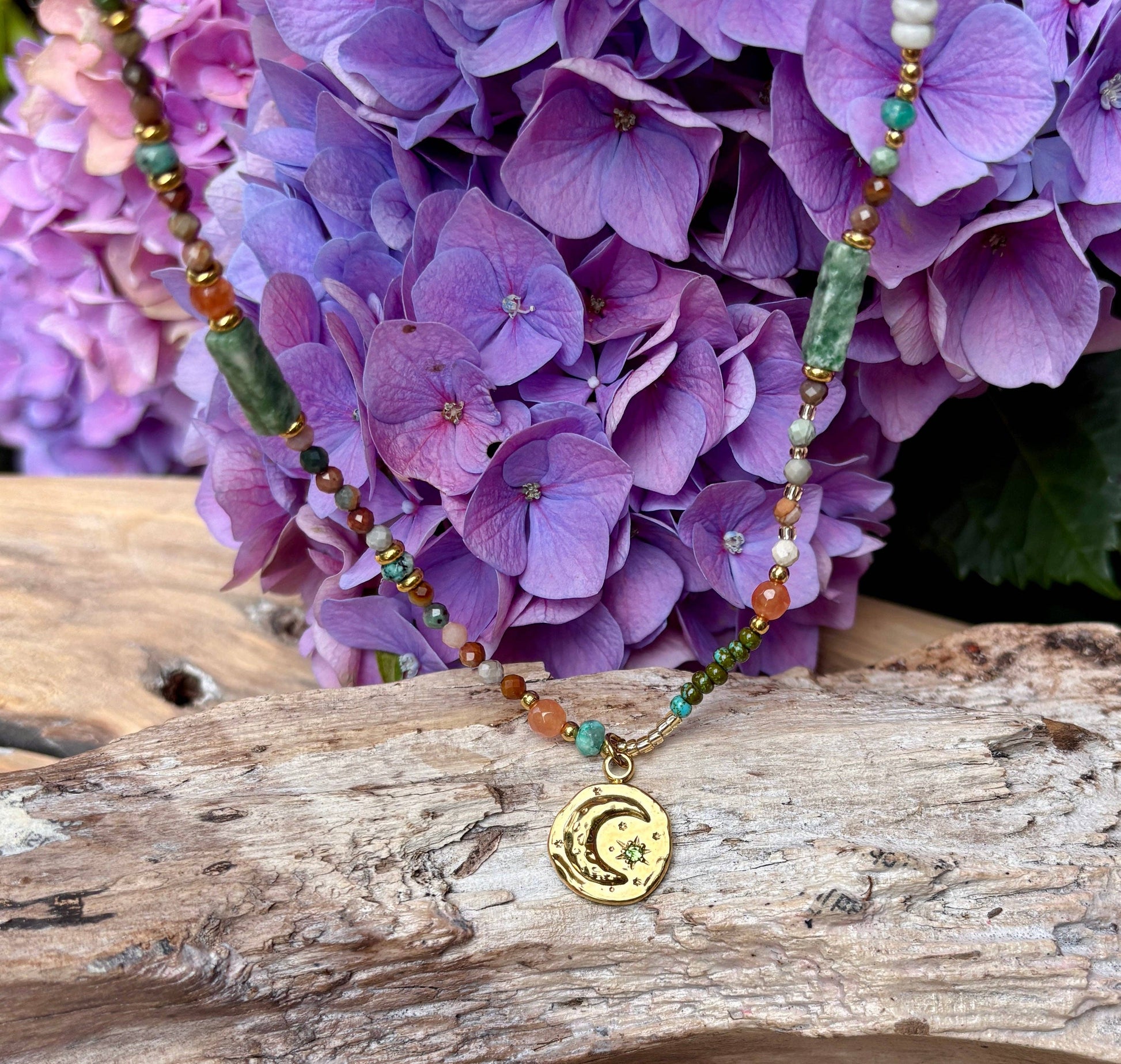 Necklace with a moon and star pendant on a wooden surface with purple flowers in the background