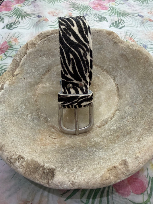 Zebra print belt on a textured stone surface with floral patterned background