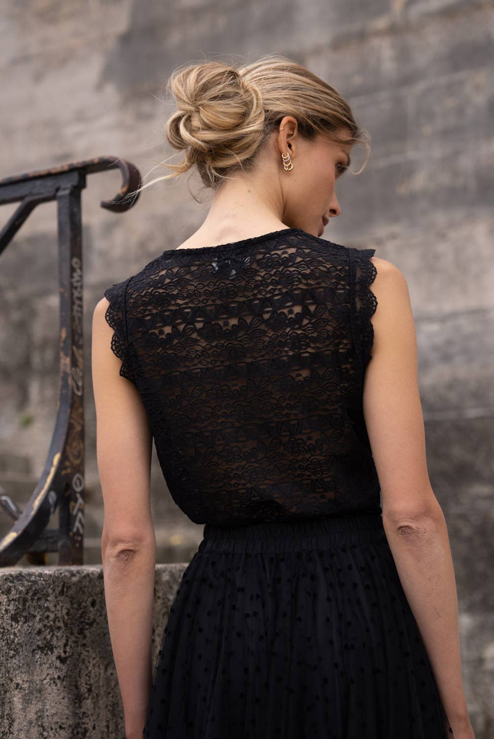 Woman wearing a black lace dress against a stone wall.