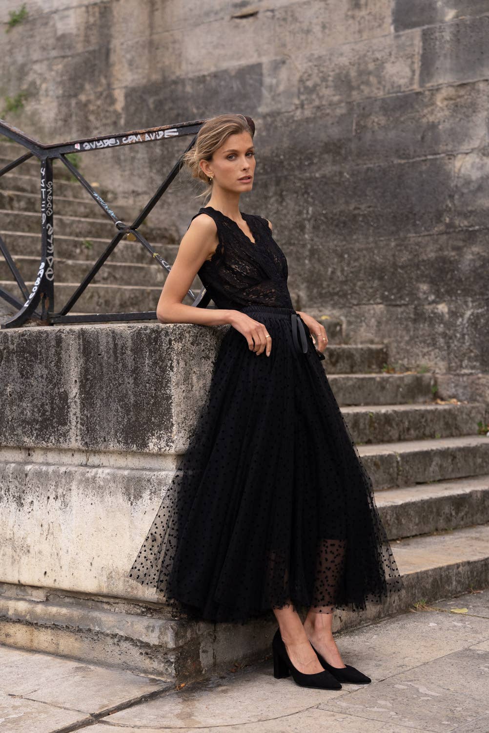 Woman in a black lace top  standing on stone steps.