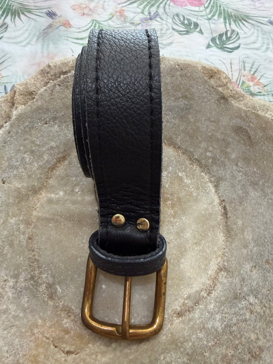 Black leather belt with a brass buckle on a stone surface