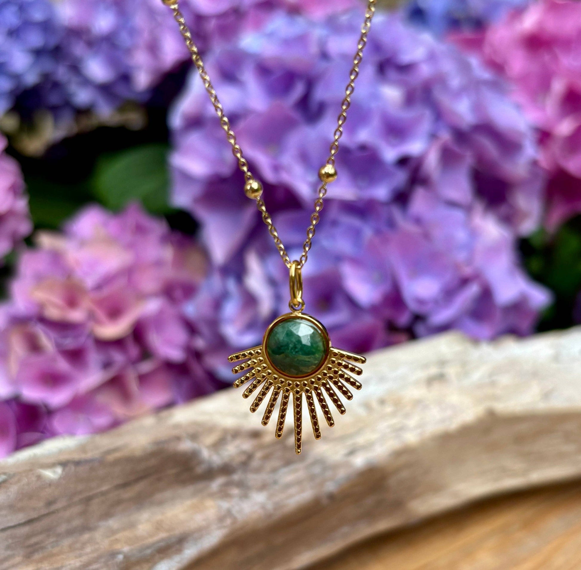 Gold necklace with a green pendant against a background of purple flowers