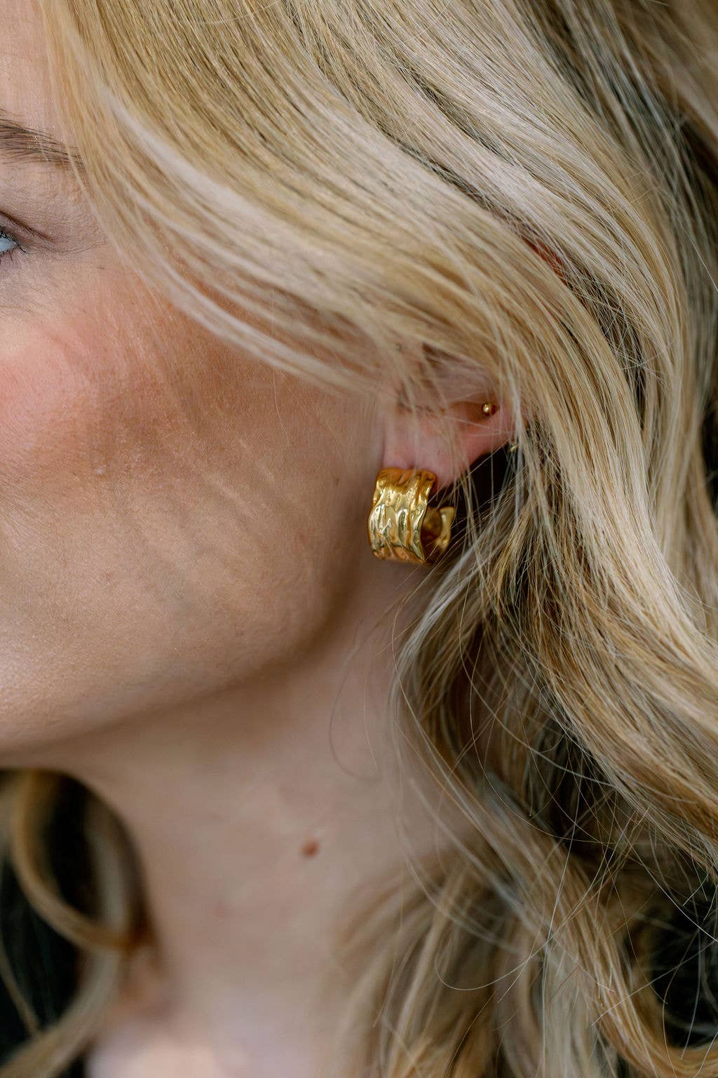 Wide textured gold hoop earring in 18kt gold-plated stainless steel with post-back fastening.