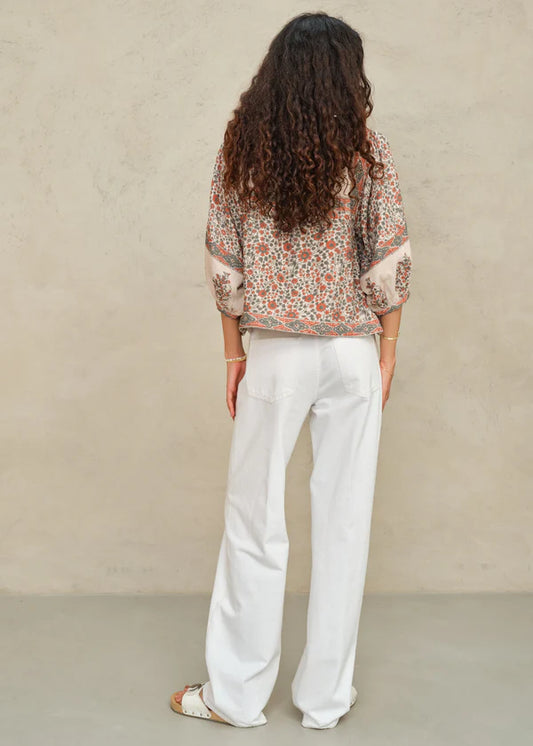 Person wearing a patterned top and white pants against a beige background