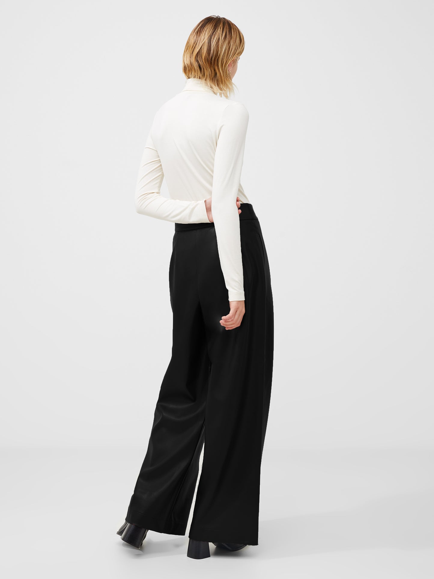 Woman wearing a cream polo neck top with split sides to the cuff.  Picture is taken from the back