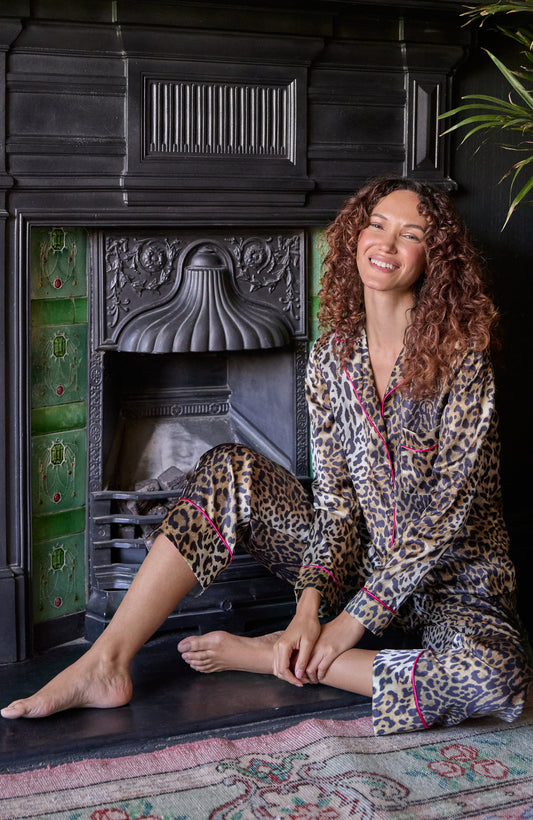 Woman in Hope & Ivy SIndy leopard print pajamas sitting in front of a fireplace.