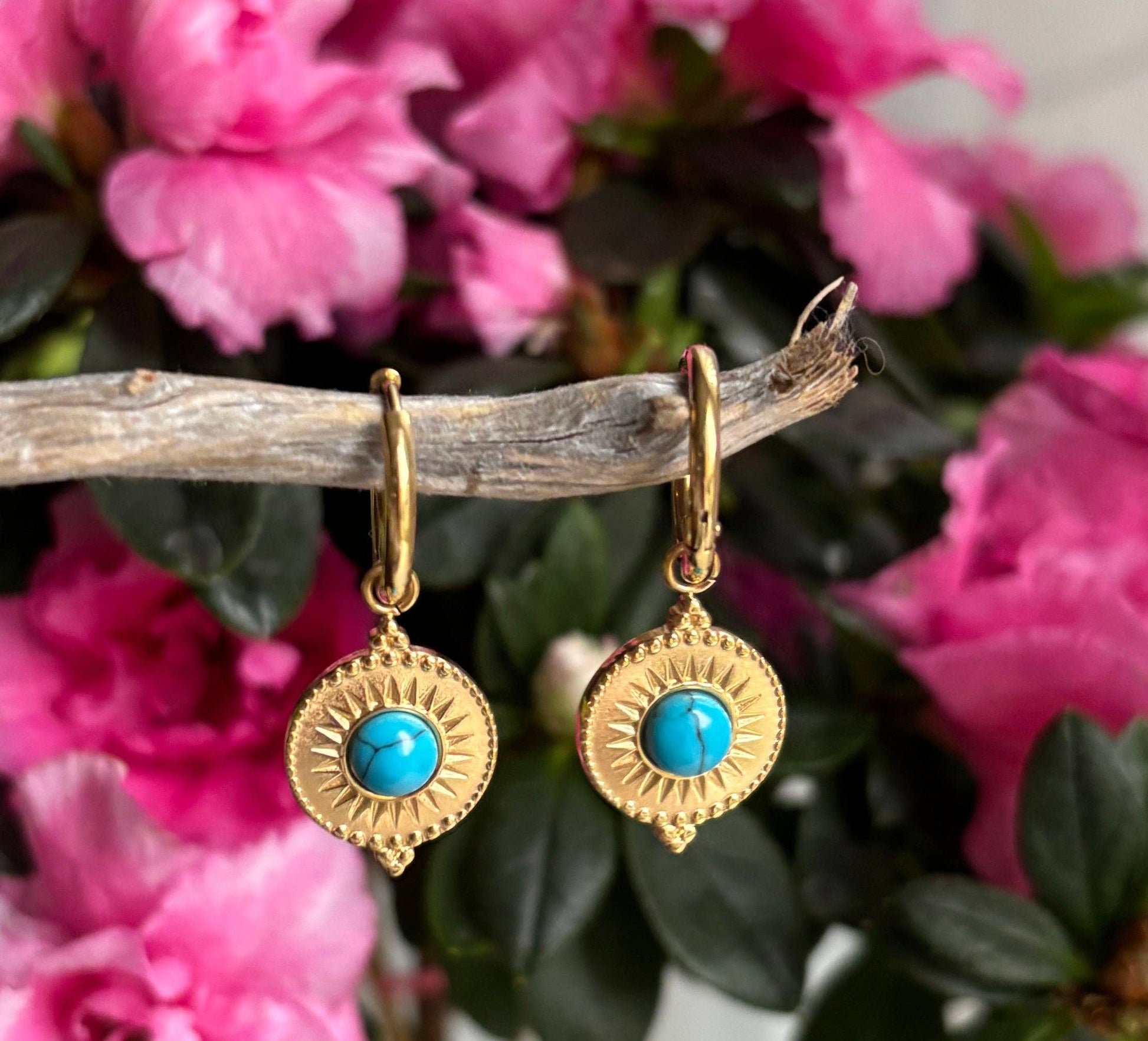 Gold earrings with turquoise stones on a branch with pink flowers in the background