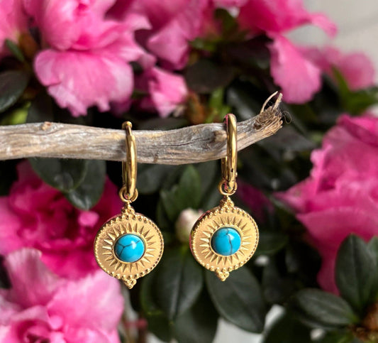 Gold earrings with turquoise stones on a branch with pink flowers in the background