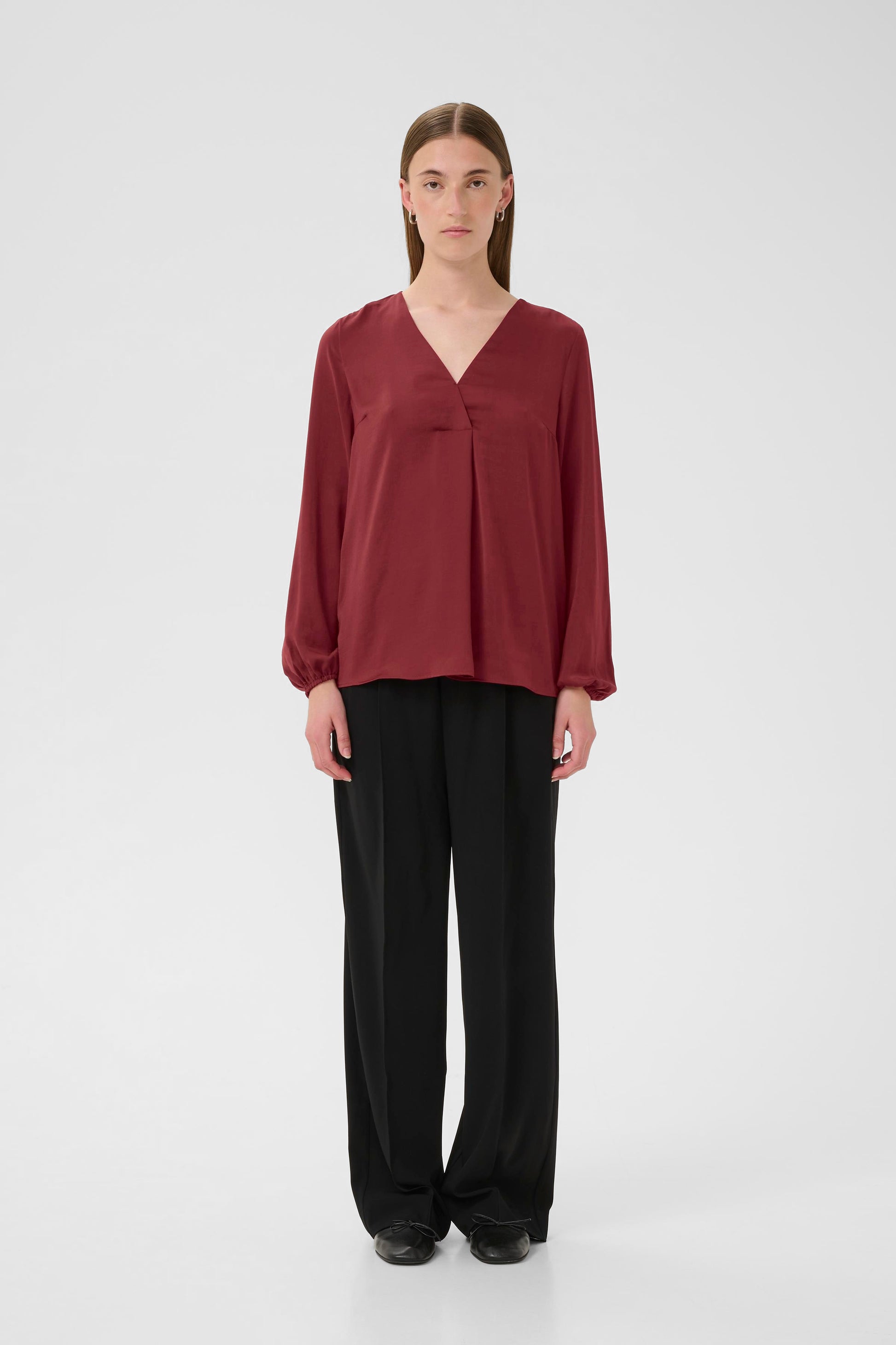 Woman wearing a burgundy Blouse with long sleeves and V Neck on a white background
