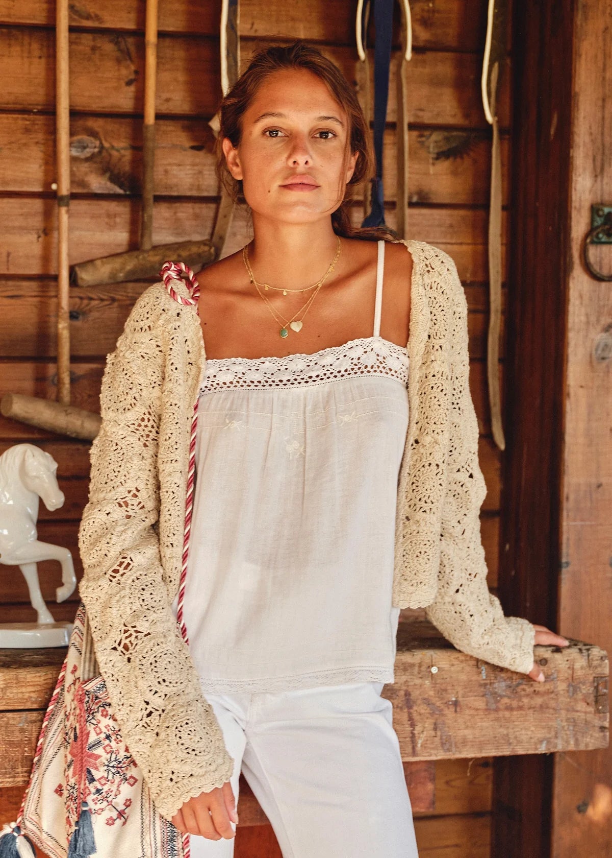 Woman wearing the M.A.B.E Maci  beige crochet cardigan over a white top in a rustic setting