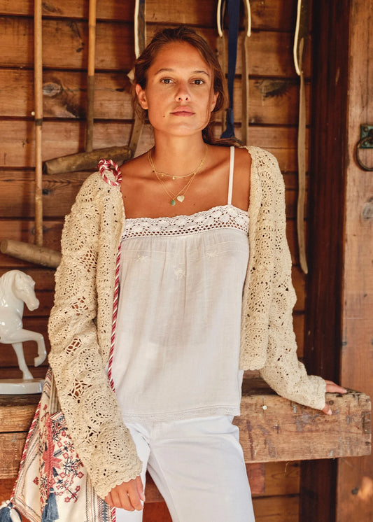 Woman wearing the M.A.B.E Maci  beige crochet cardigan over a white top in a rustic setting