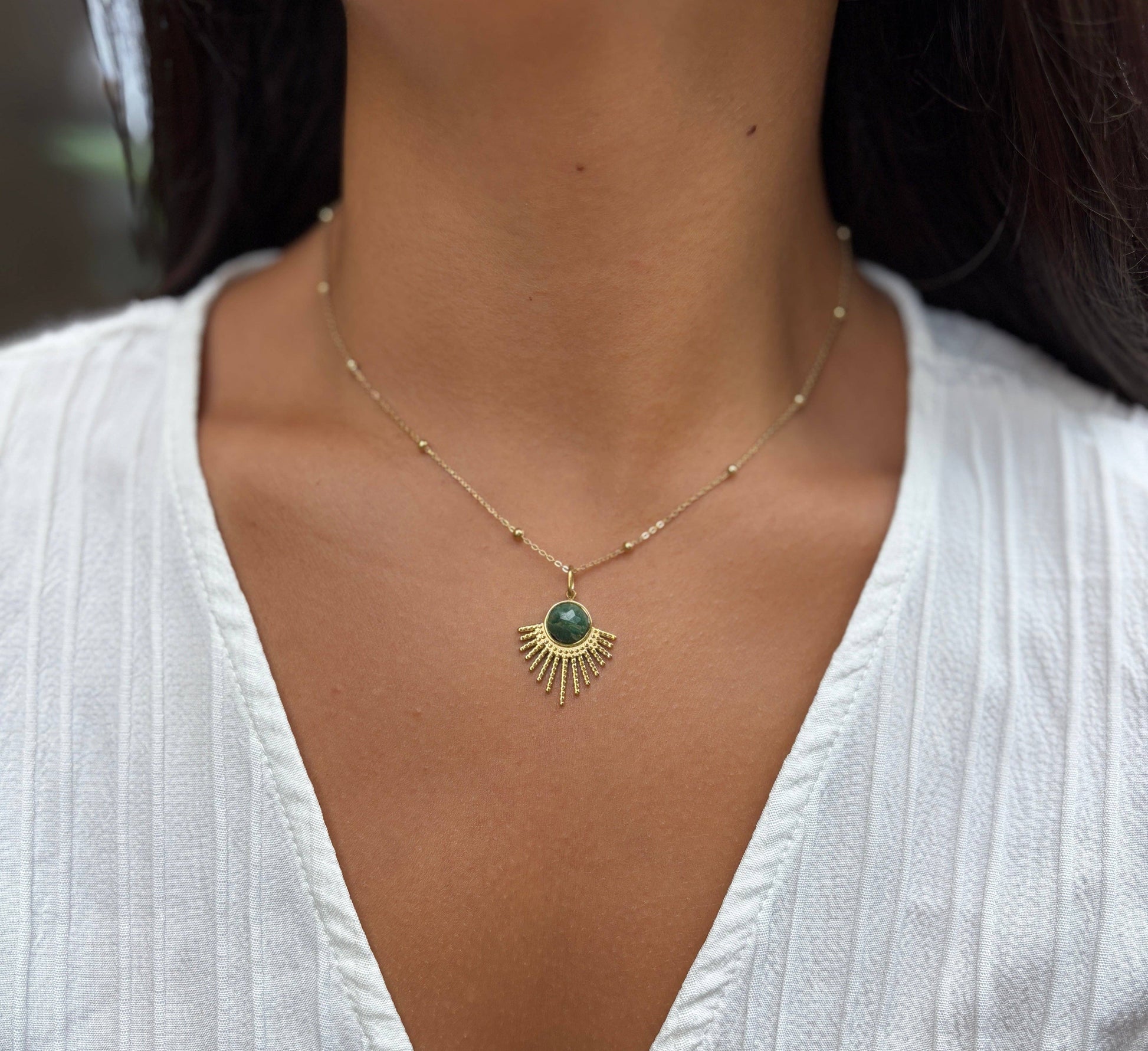 Necklace with a green pendant worn by a person in a white top