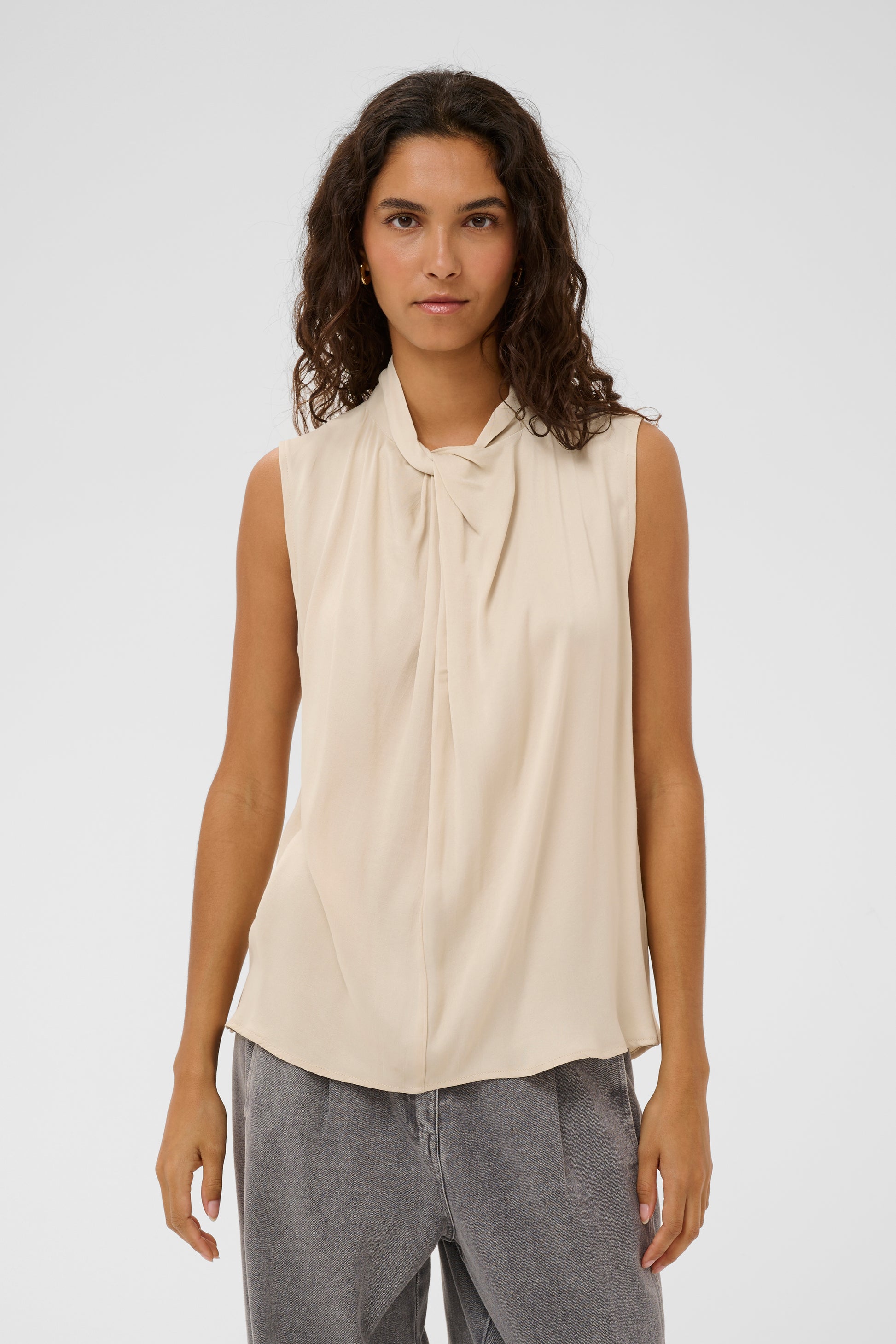 Woman wearing the soaked in luxury nadeya miria  beige sleeveless blouse with a tie neckline.