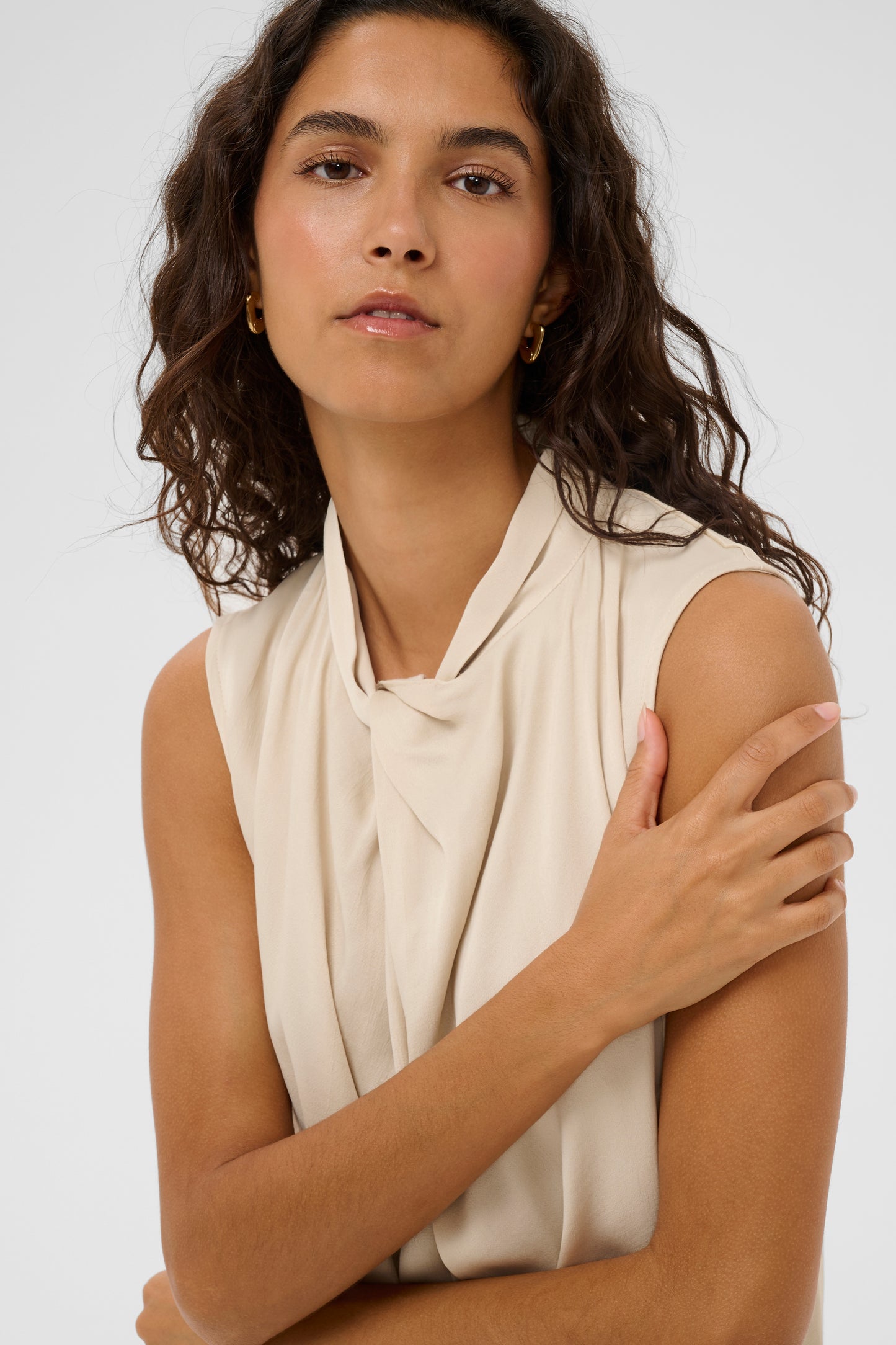 Woman wearing the soaked in luxury nadeya miria  beige sleeveless blouse with a tie neckline.