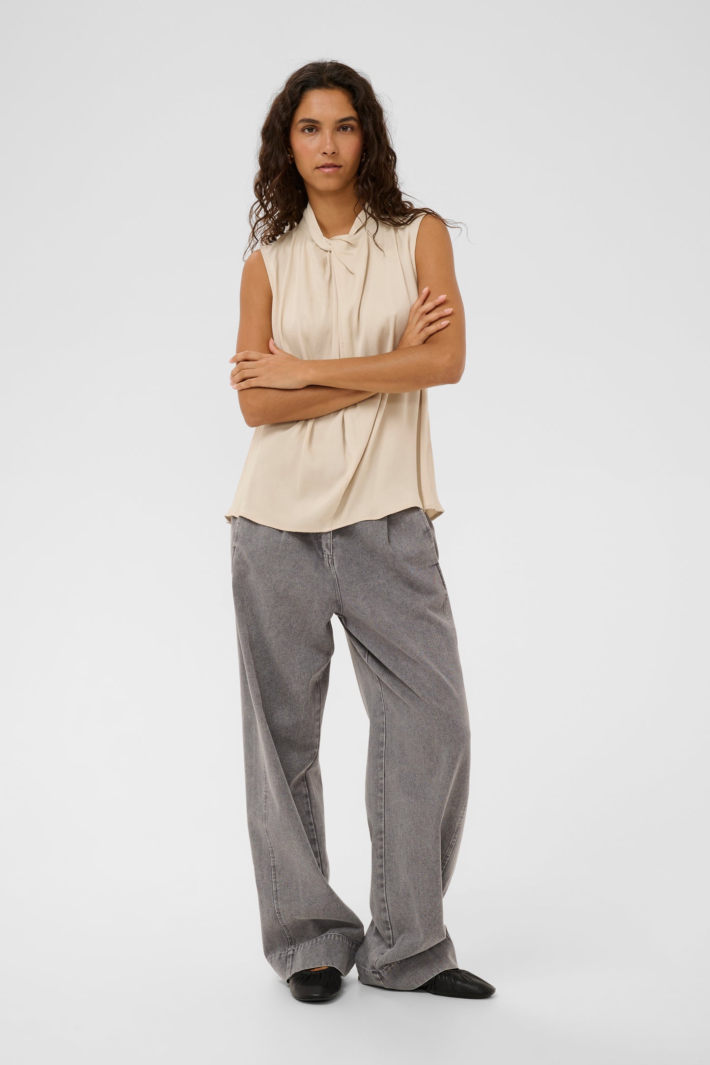 Woman wearing the soaked in luxury nadeya miria  beige sleeveless blouse with a tie neckline.