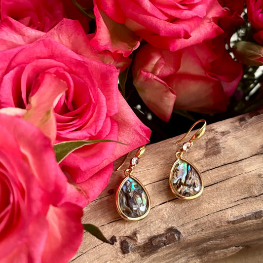 Ocean Ripples Gold  and Abalone teardrop earrings on a piece of wood with roses around it