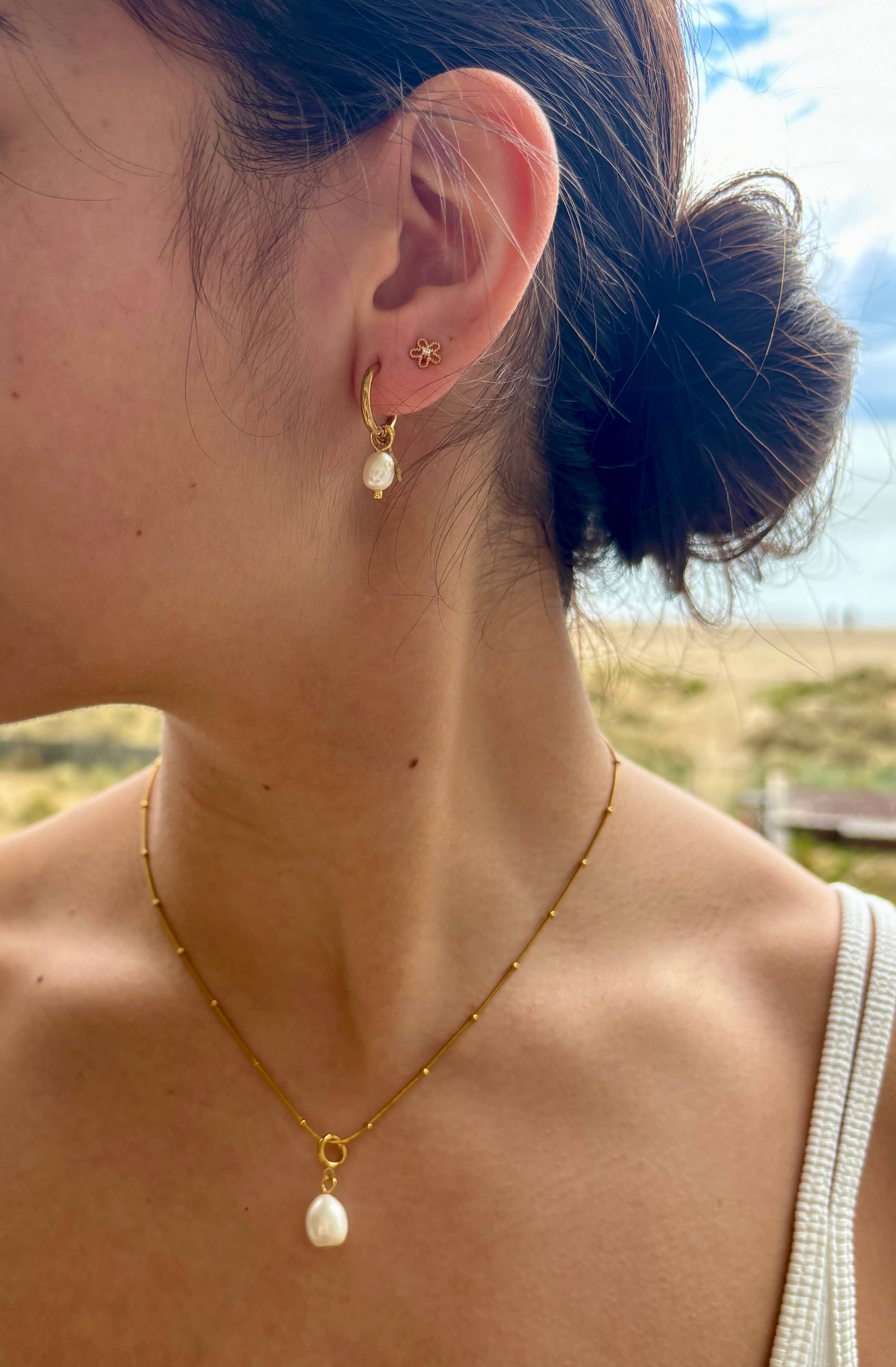 Close-up of a person wearing gold hoop earrings with pearl accents and a matching necklace.