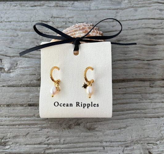 Gold earrings with pearl accents on a 'Ocean Ripples' branded card against a wooden background
