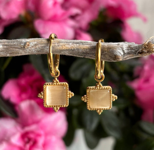 Gold plated square earrings with a clear quartz on a branch with pink flowers in the background