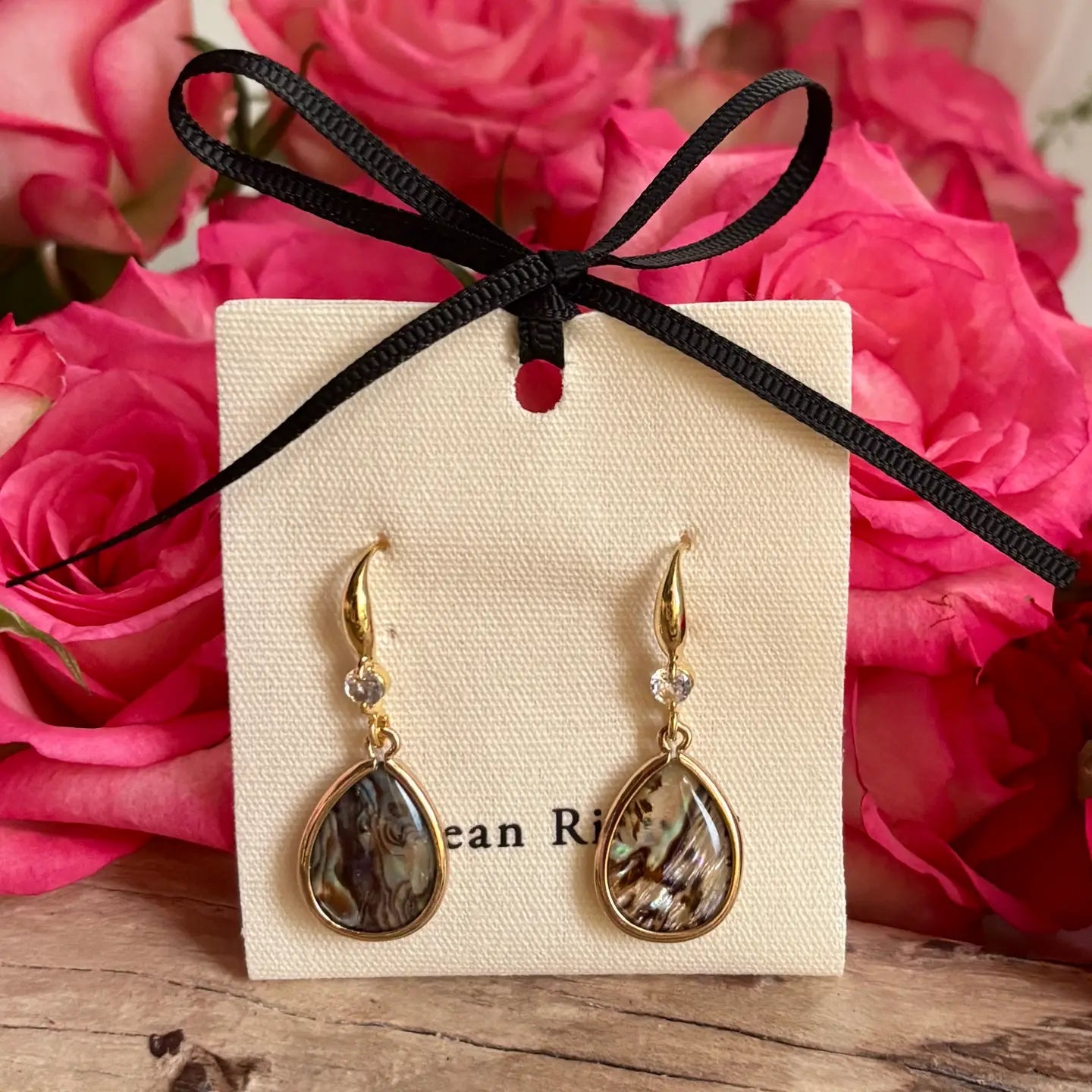 Ocean Ripples Gold  and Abalone teardrop earrings on a branded card with pink roses in the bbackground