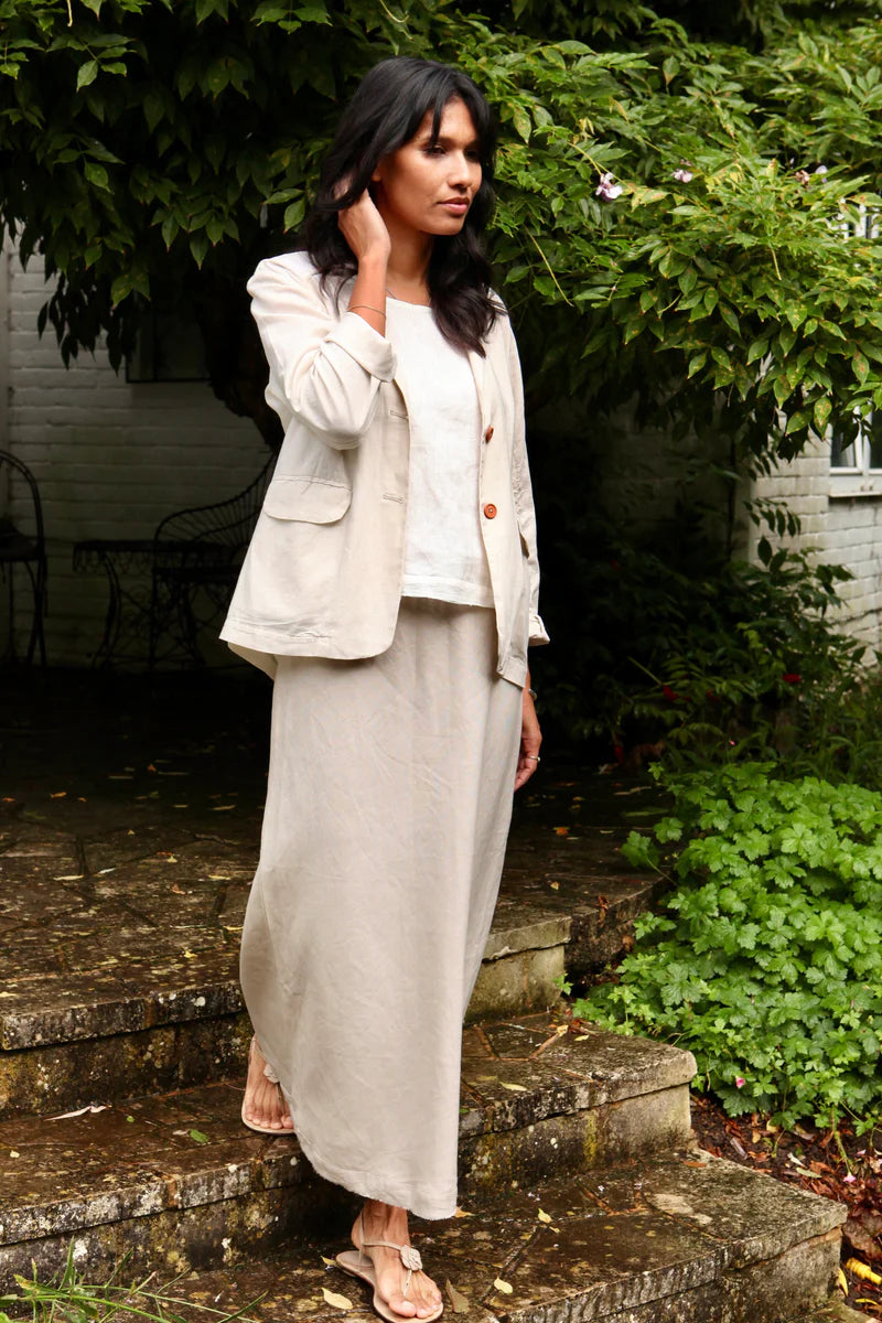 Woman in a beige outfit standing on stone steps with greenery around