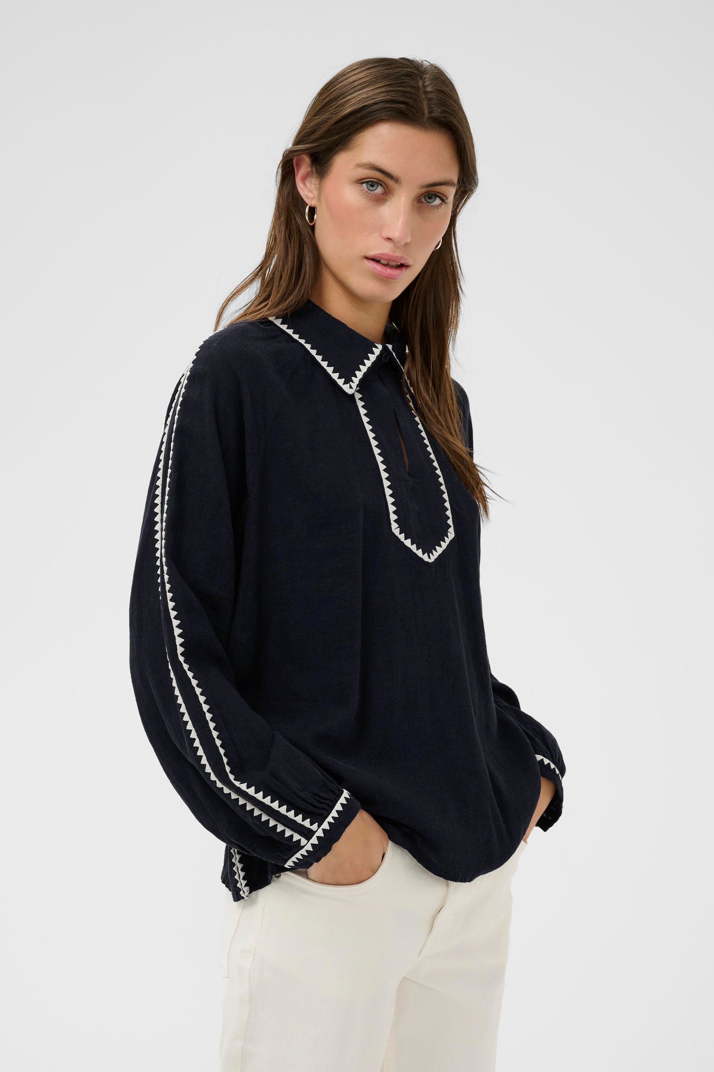 Woman wearing the part two Aimy Linen blend navy  blouse with white trim and white pants on a white background
