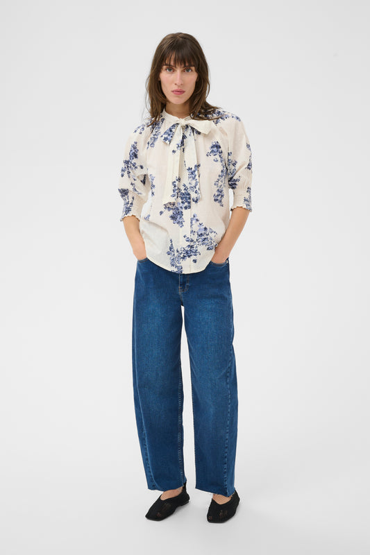 Woman wearing the Part Two Almera blue and white floral blouse and blue jeans on a white background