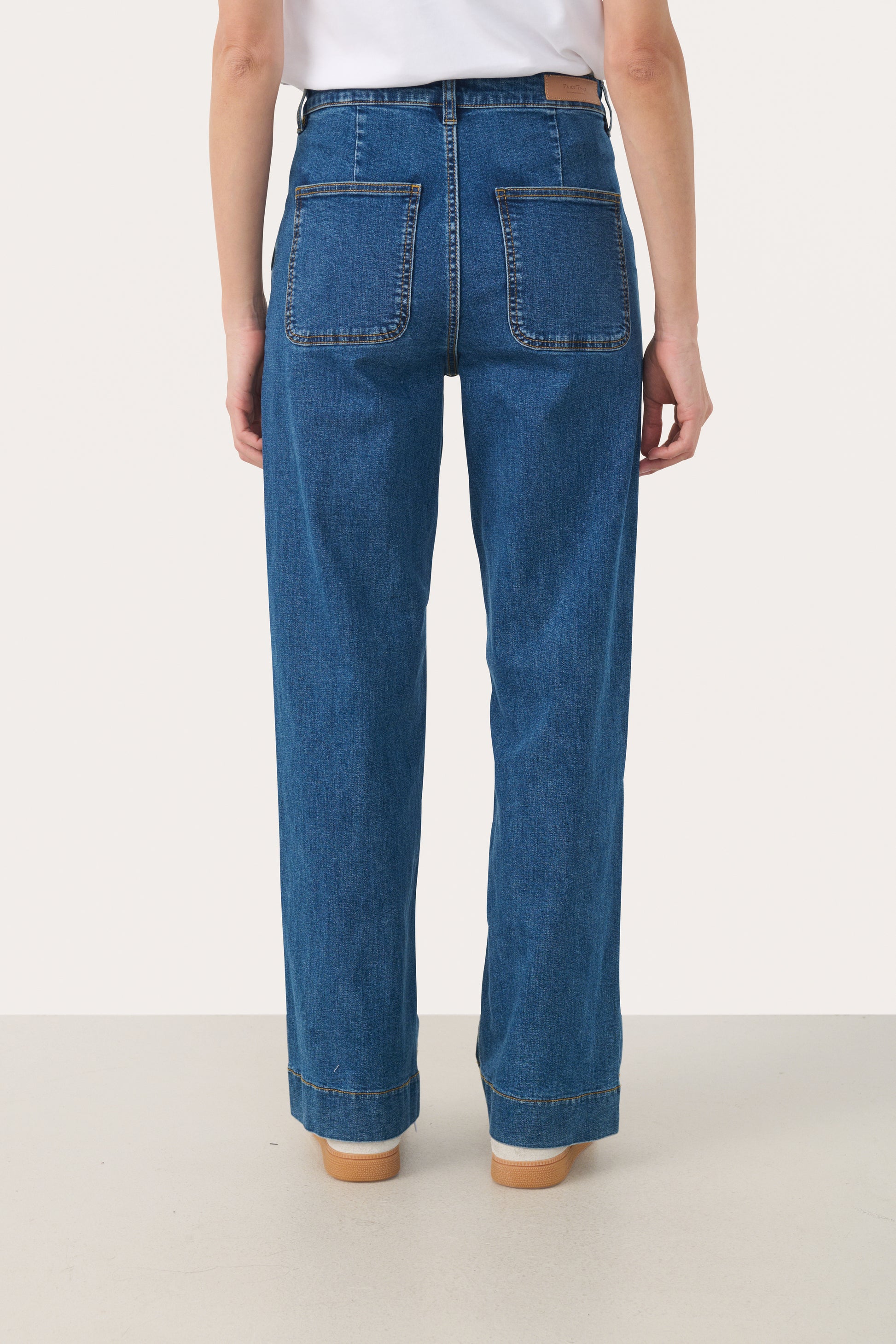 Woman wearing straight leg jeans in a medium blue wash with a white t-shirt.  View from the back showing 2 pockets