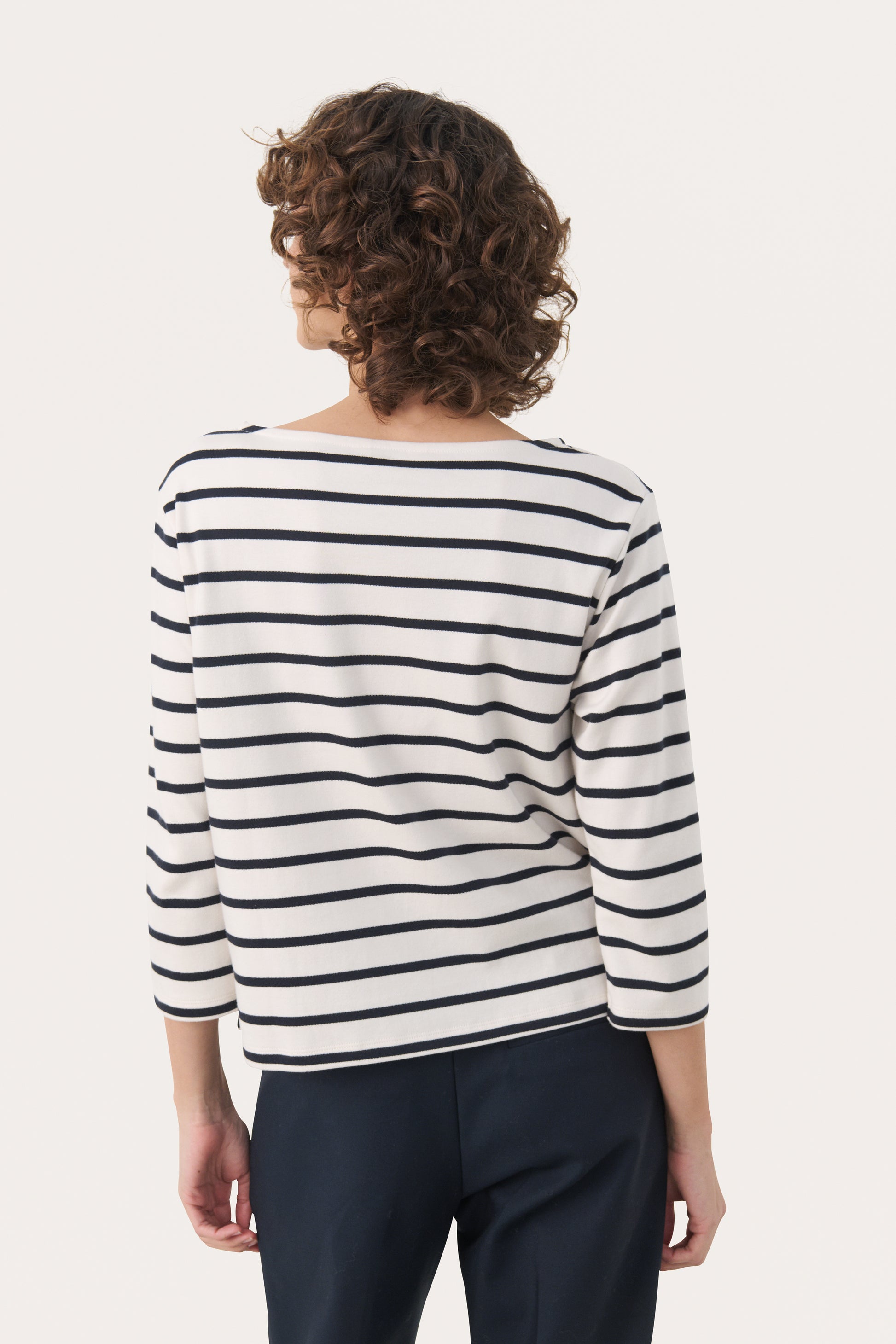 Woman wearing a 3/4 length sleeve white top with dark navy stripes. Back View