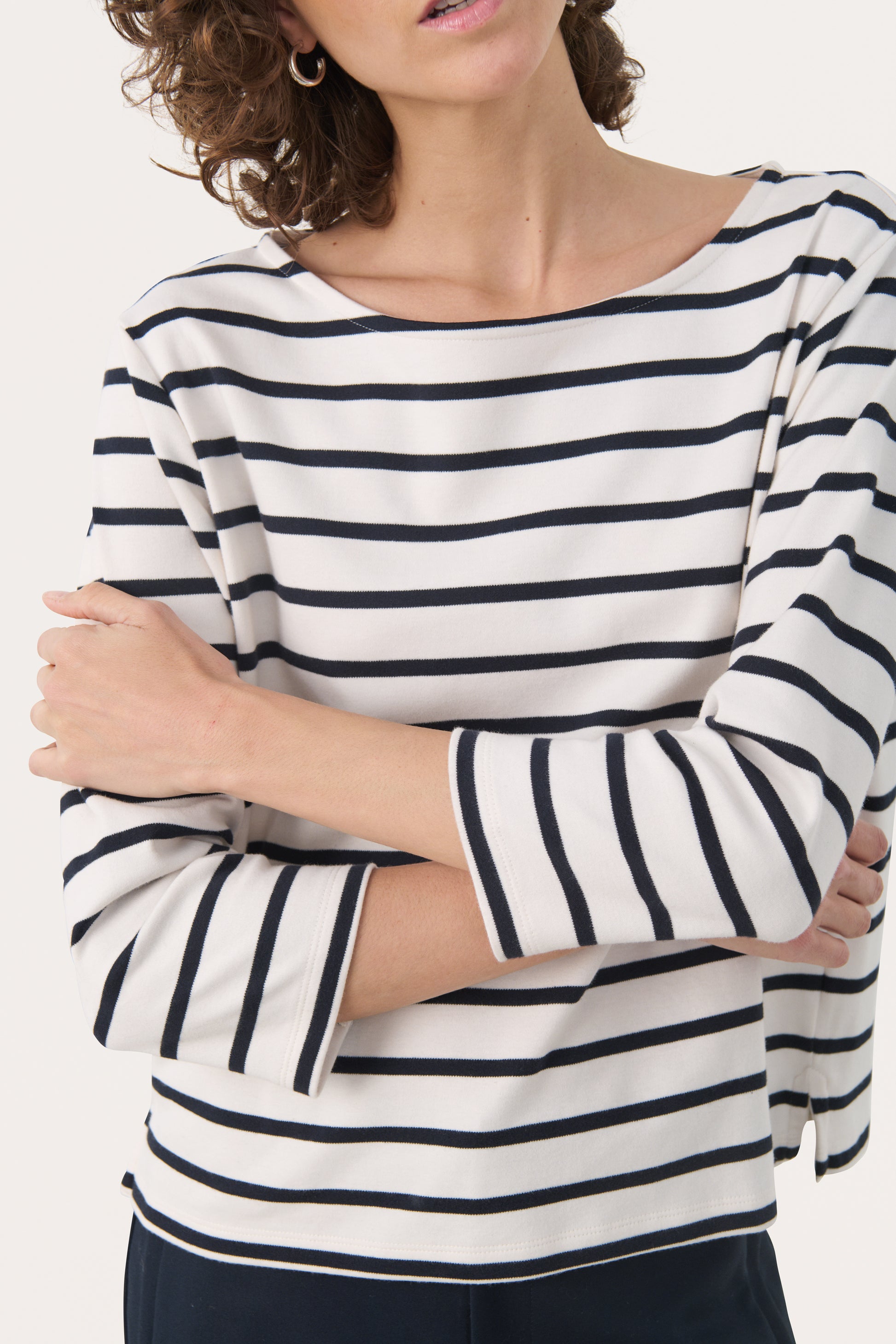 Woman wearing a 3/4 length sleeve white top with dark navy stripes. 
