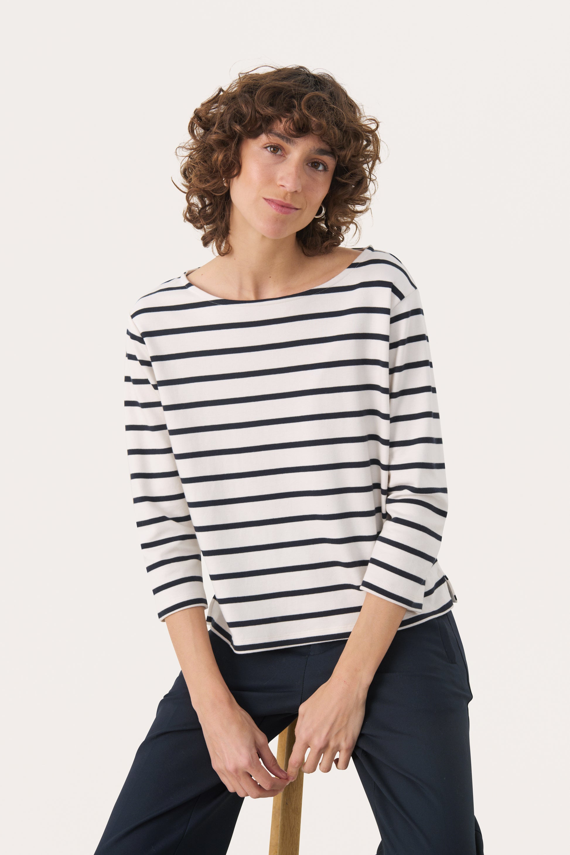 Woman wearing a 3/4 length sleeve white top with dark navy stripes. 