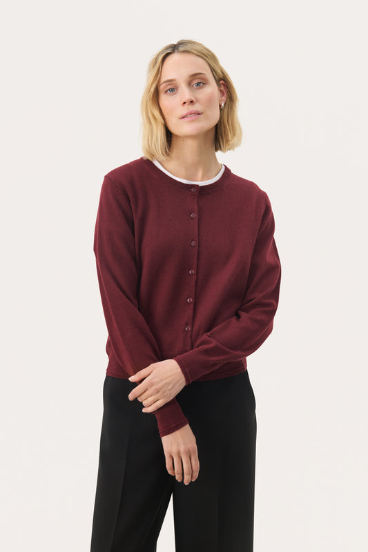 Woman wearing a small button cardigan in a deep port/red colour.  