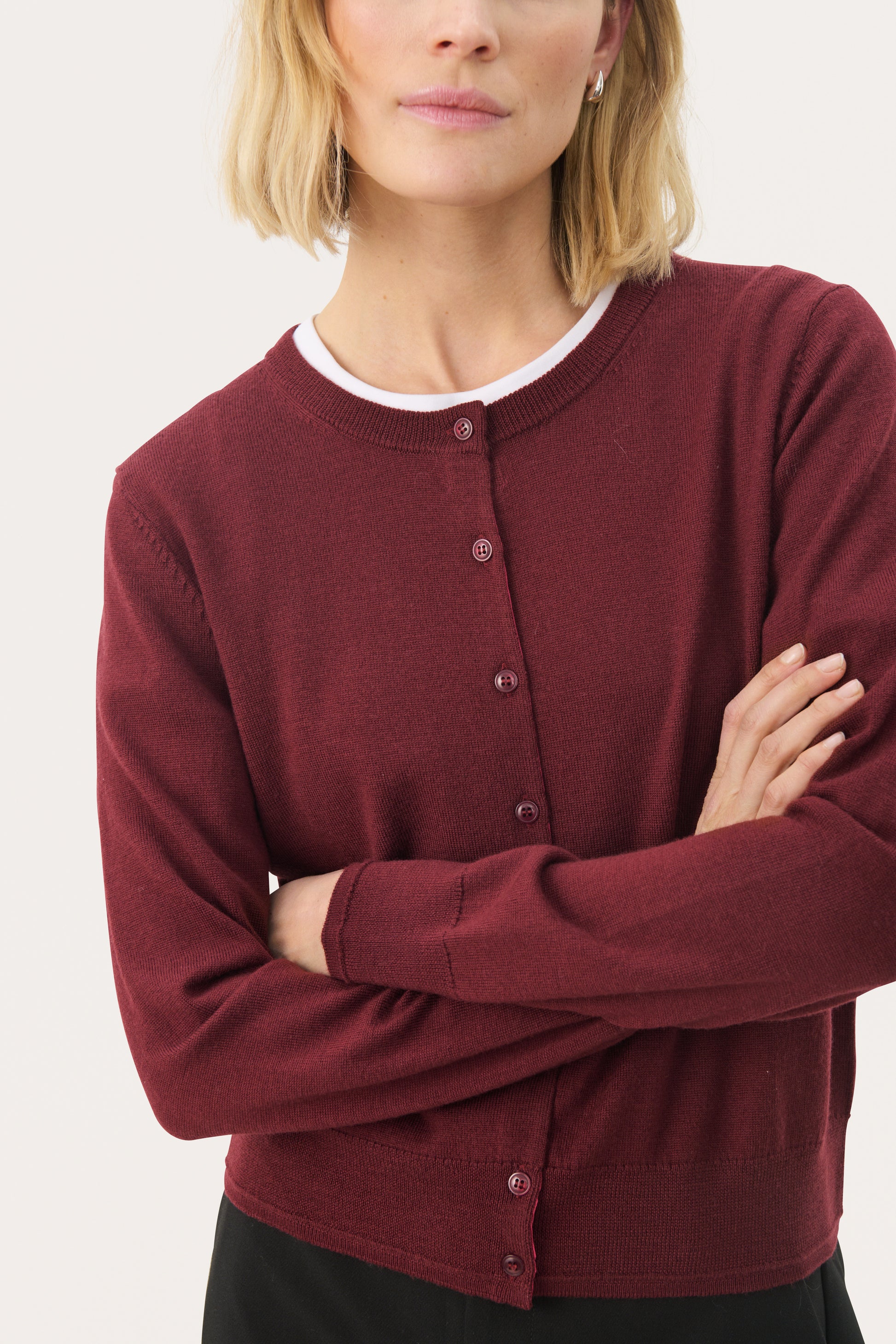 A woman wearing a tawny port colored, long-sleeved, button-up cardigan over a white top, paired with black pants.