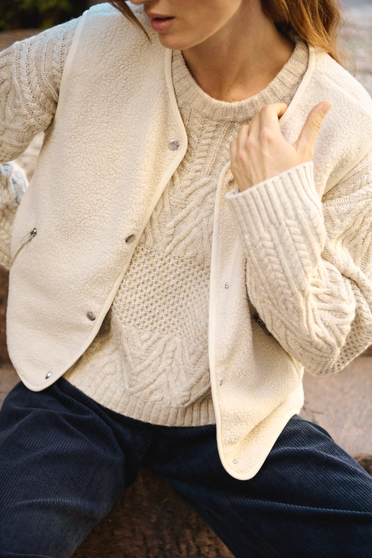 Woman wearing a knitted oatmeal jumper layered with a knitted oatmeal waistcoat with silver buttons and pockets