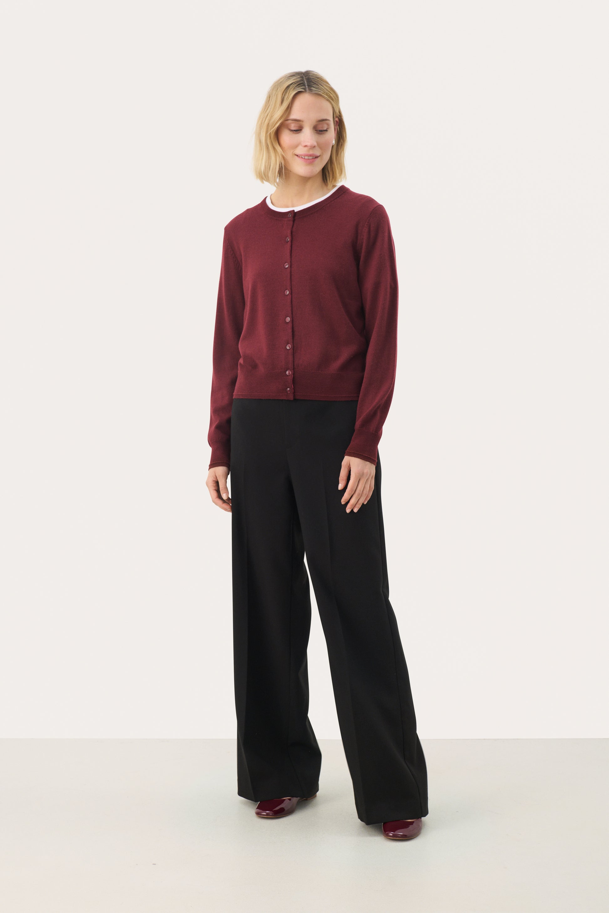 Woman wearing a small button cardigan in a deep port/red colour.  