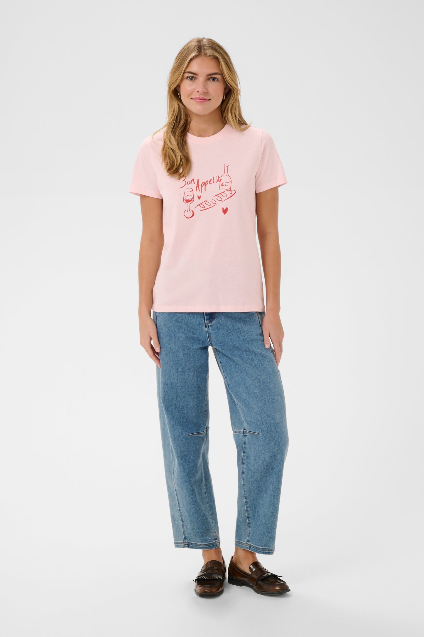 Woman wearing a pink t-shirt with text and blue jeans on a white background