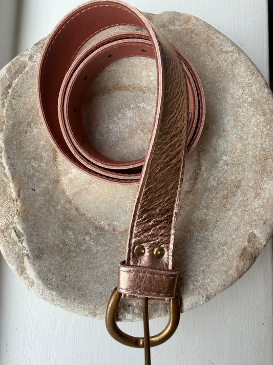 Rose gold belt with a gold buckle on a stone surface