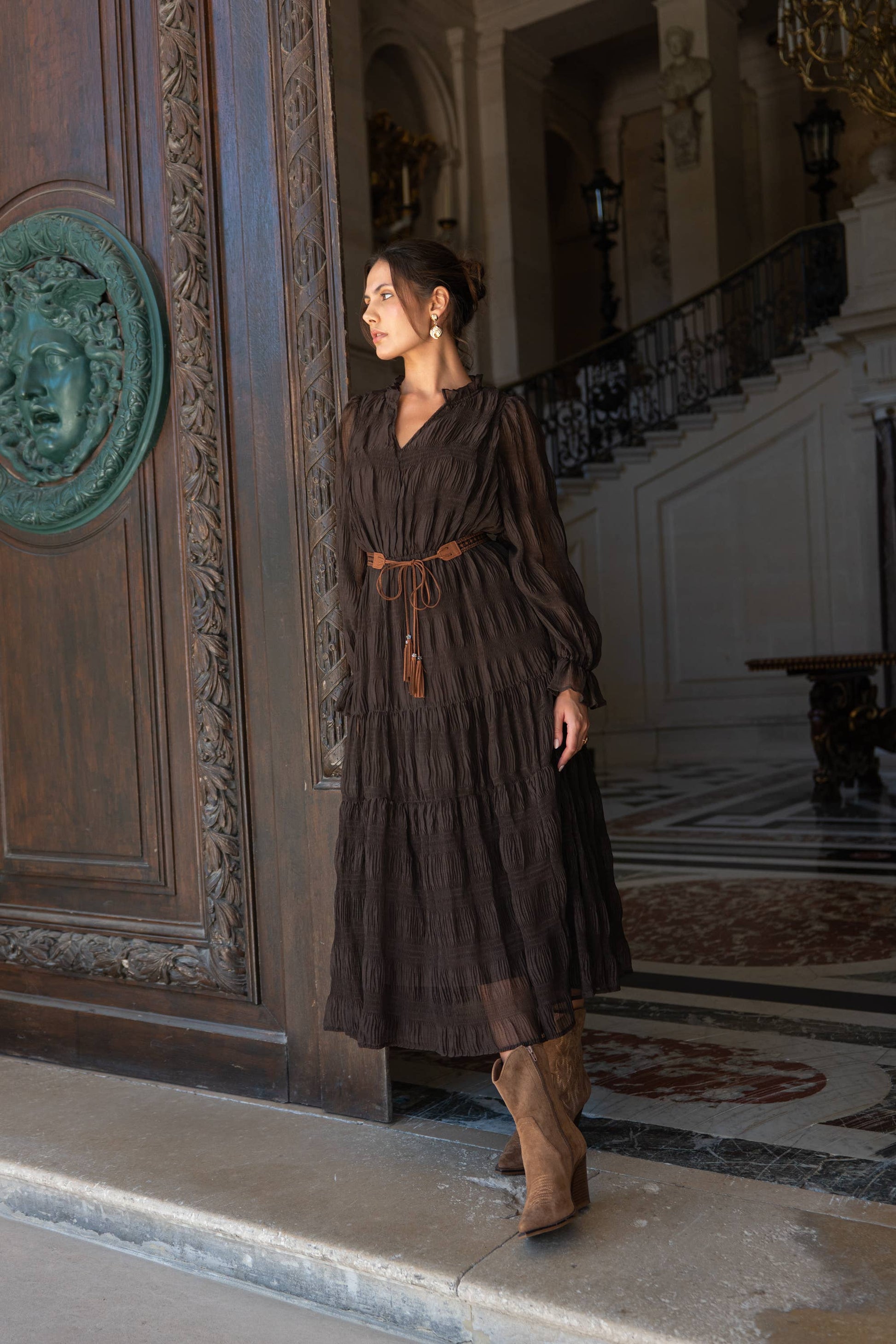 Woman wearing a long ruched brown dress with long chiffon sleeves
